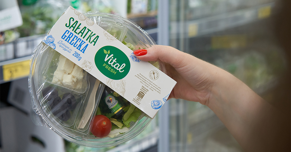 Customer's hand holding a packaged Vital Fresh greek salad in a store (photo)
