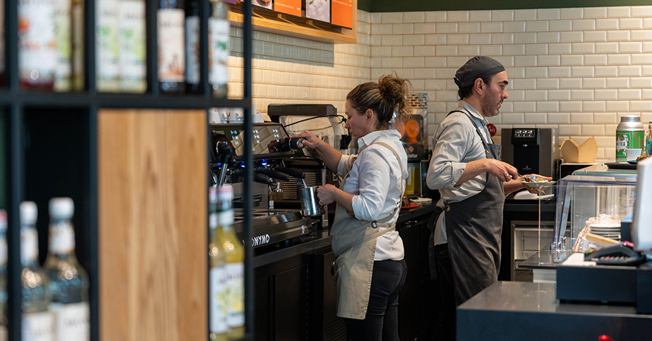 Two employees in a Jeronymo store making coffee and serving cake (photo)