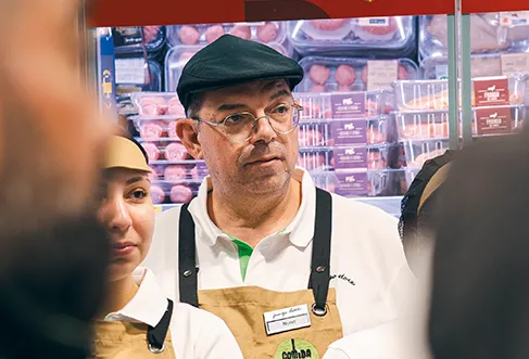 A group of Pingo Doce employees with Comida Fresca aprons standing in front of the refrigerated meat section. The photo is taken over the shoulder of two of the employees (photo)