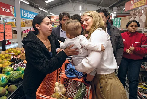 A woman hands over a baby to another woman in an Ara store full of customers (photo)