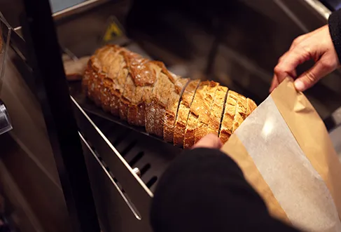 Freshly cut bread at a store that is being put into a paper bag (photo)