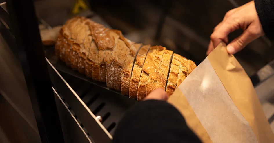 Freshly cut bread at a store that is being put into a paper bag (photo)
