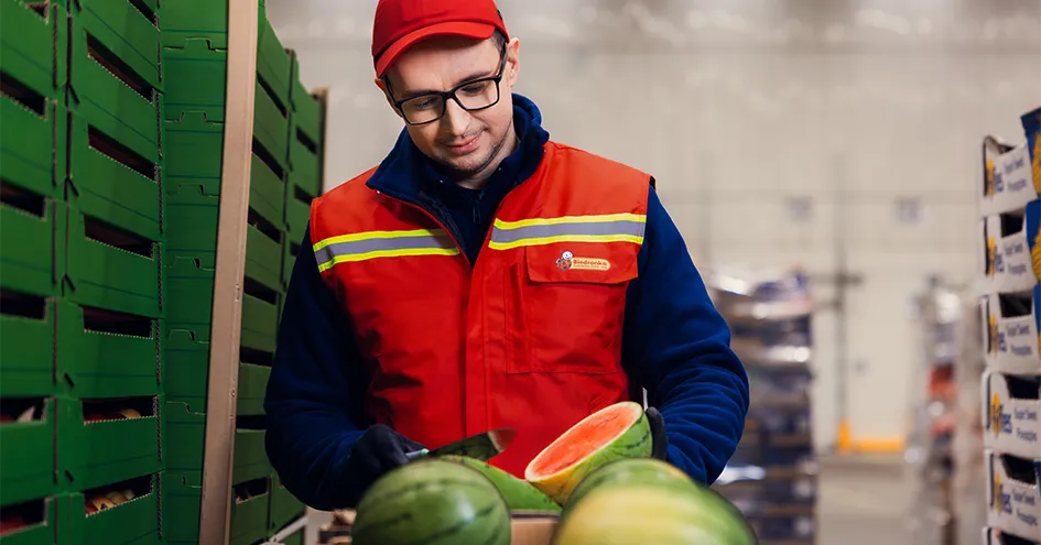Biedronka employee cutting a watermelon in a distribution centre. Further crates can be seen to the side and in the background. (photo)