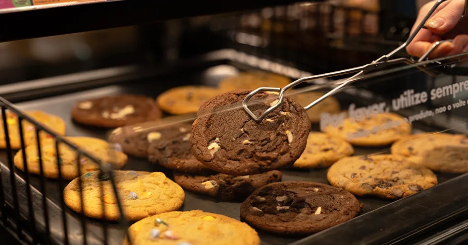 Close-up of chocolate-chip cookes. One cookie is being picked up with a pair of tongs. (photo)