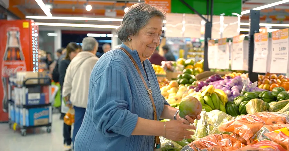 An elderly lady taking a mango from the fruit shelf in a store (photo)