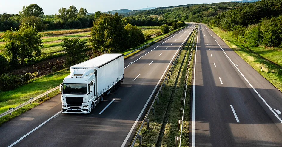 A truck on a road on a sunny day. There's green landscape on both sides of the road. (photo)