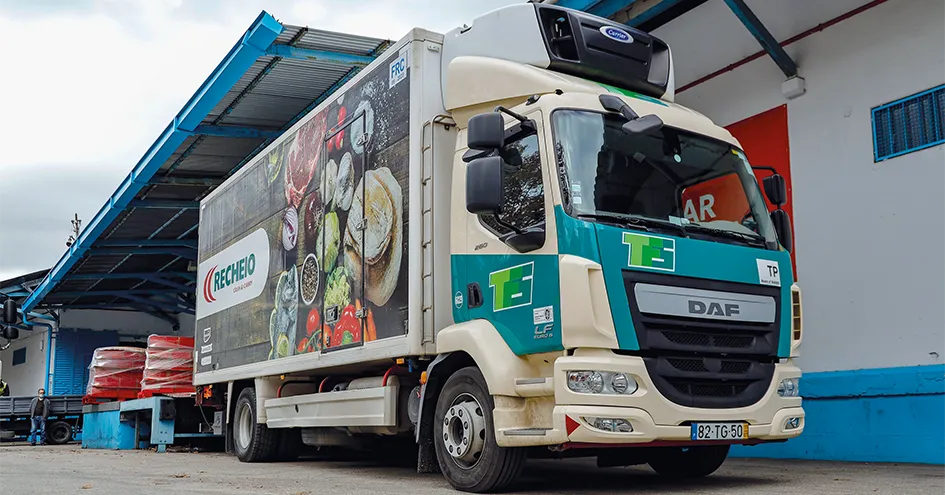 A deliver truck in a loading bay. On the side of the truck is a photo of various fresh products and the Recheio logo. (photo)