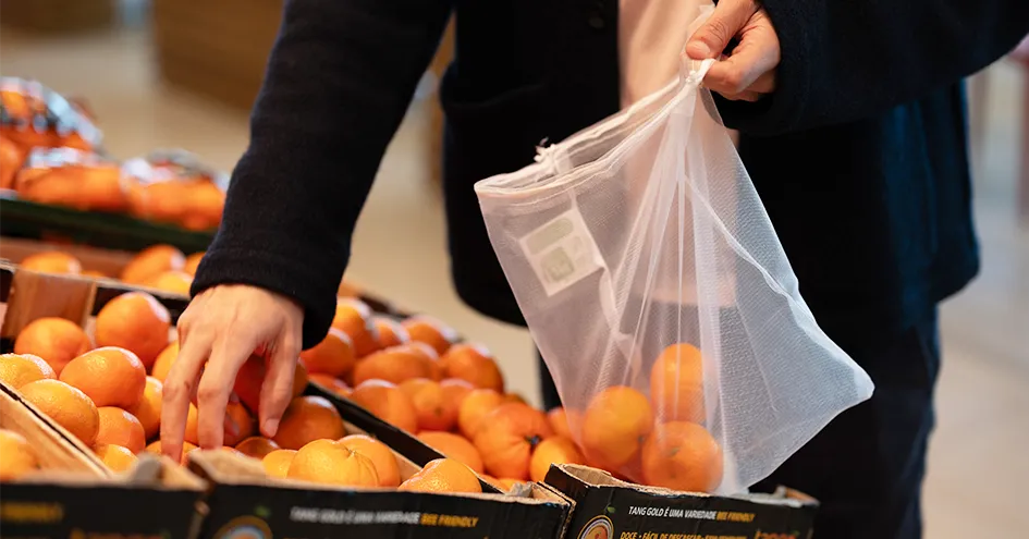 Close-up showing a person picking mandarins in a store and placing them in a reusable bag (photo)