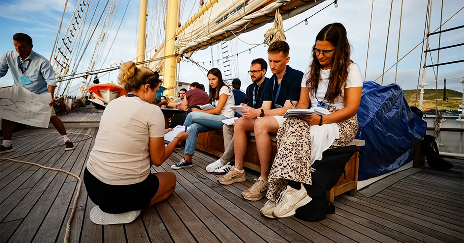Young adults sitting on a bench in the centre of Santa Maria Manuela ship and taking notes (photo)