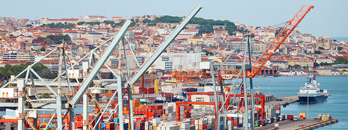 Porto com gruas em primeiro plano e um navio e colinas cobertas de edifícios ao fundo (foto)