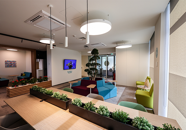 Espaço de lounge luminoso com plantas, mobiliário confortável, candeeiros diferentes e um ecrã na parede (foto)