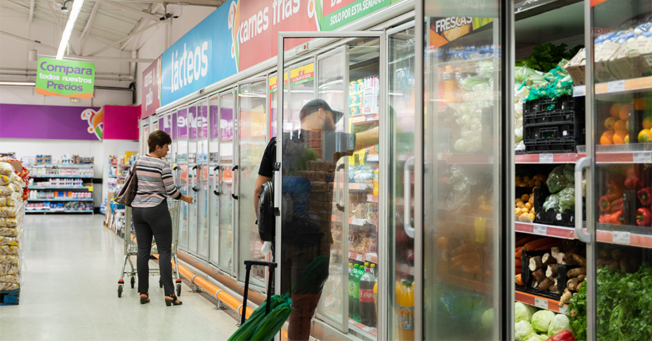 Dois clientes num supermercado em frente a prateleiras refrigeradas (foto)