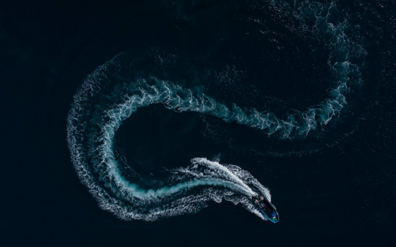 Pequeno barco visto de cima deixando um rasto em forma de S na água (foto)