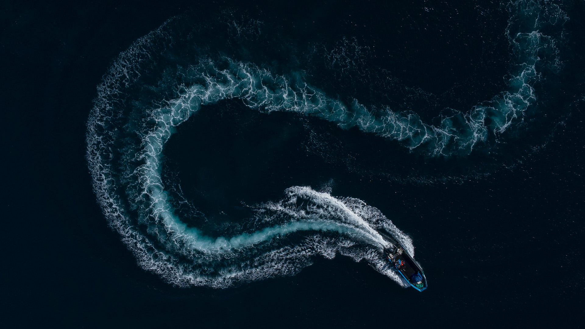 Pequeno barco visto de cima deixando um rasto em forma de 