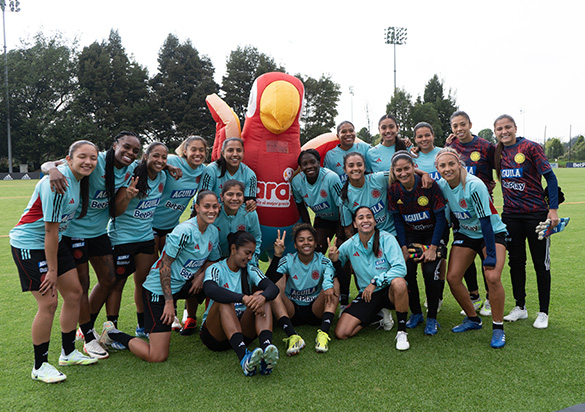 Equipa de futebol feminina no campo a posar para uma fotografia de grupo com a mascote da Ara (foto)