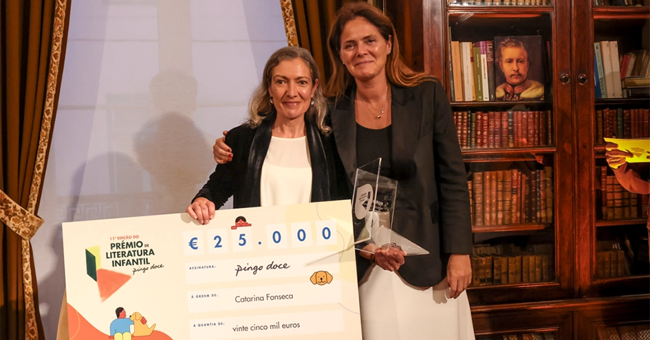 Duas pessoas numa biblioteca segurando um cheque de mais de 25.000 euros emitido pelo Pingo Doce e um troféu (foto)