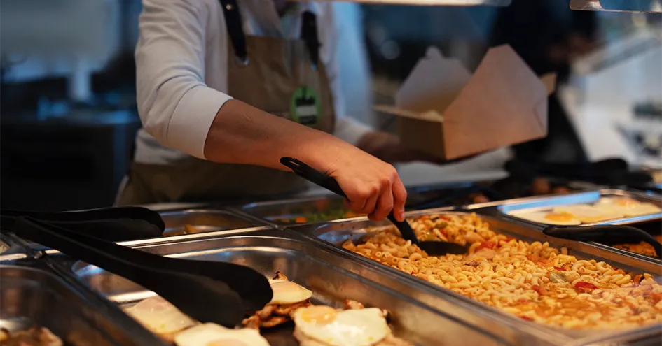 Colaborador da Comida Fresca a colocar uma refeição à base de massa numa embalagem de cartão para takeaway (foto)