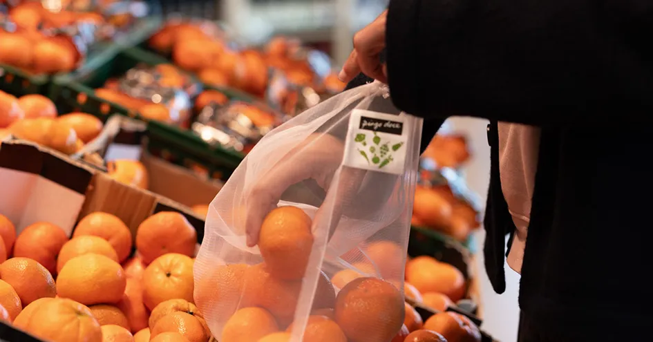 Grande plano a mostrar uma pessoa a escolher tangerinas numa loja e a colocá-las num saco reutilizável (foto)